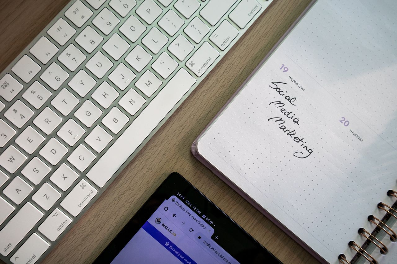 Vue de dessus d’un clavier, d’un agenda avec une note de marketing sur les réseaux sociaux et d’une tablette posés sur un bureau.